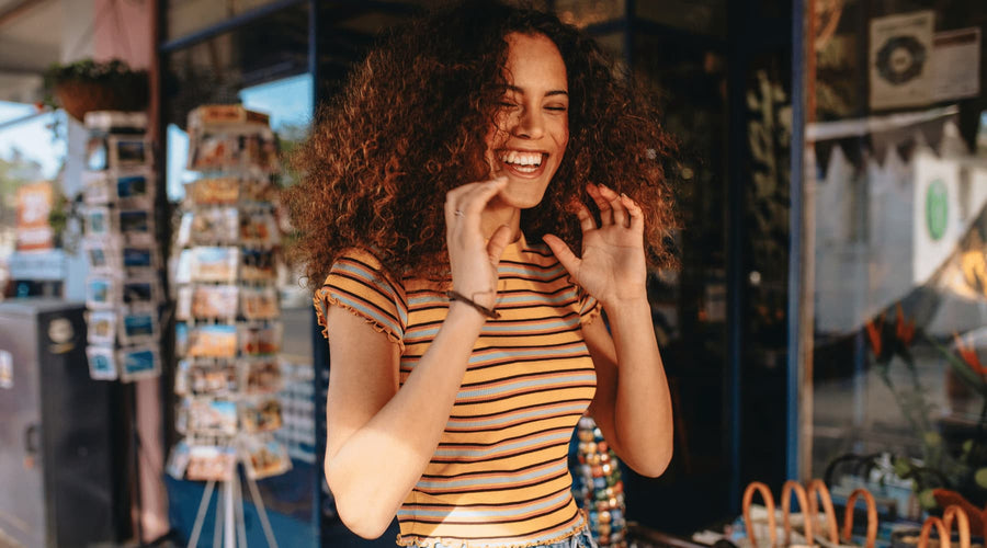 Jeune femme métisse au cheveux bouclé frisé volumineux qui sourit devant un magasin