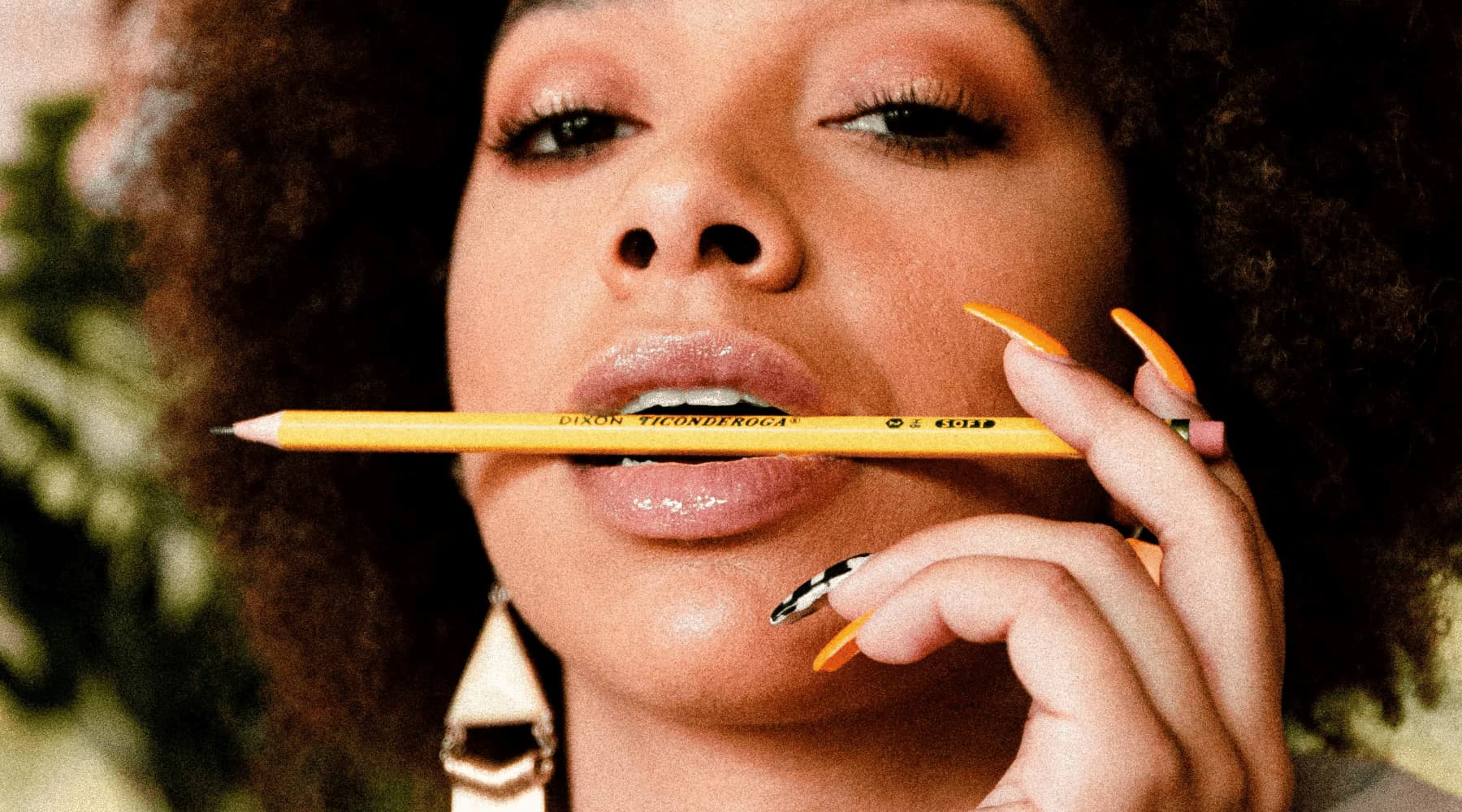 Saison des pluies photo de couverture article blog sur comment prendre soin de ses cheveux crépus pour la rentrée. Photo d'une femme afro- caribéenne aux ongles ling portant un crayon à sa bouche