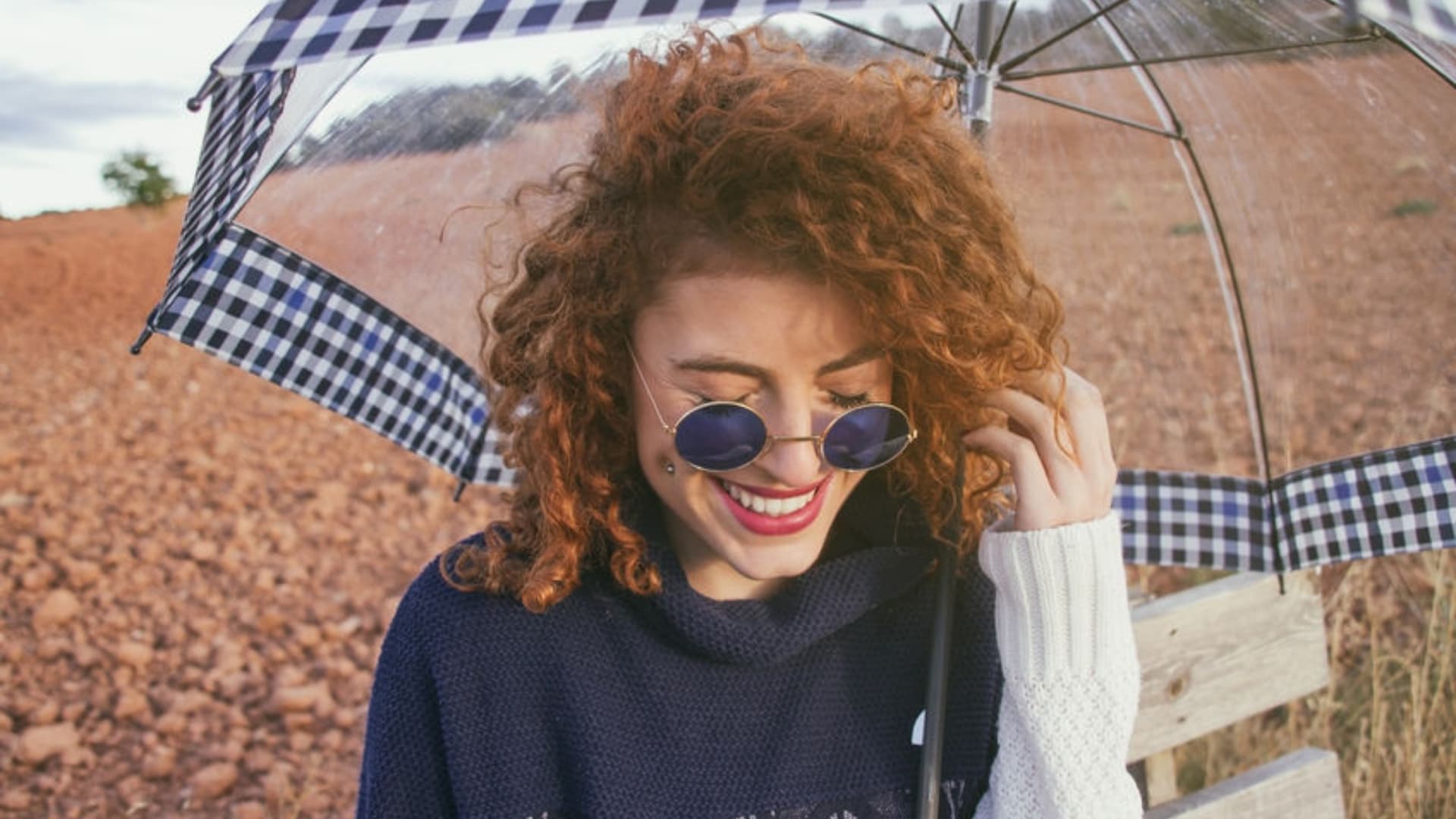 femme aux cheveux ondulés bouclés roux sur une plage rocailleuse tenant un parapluie